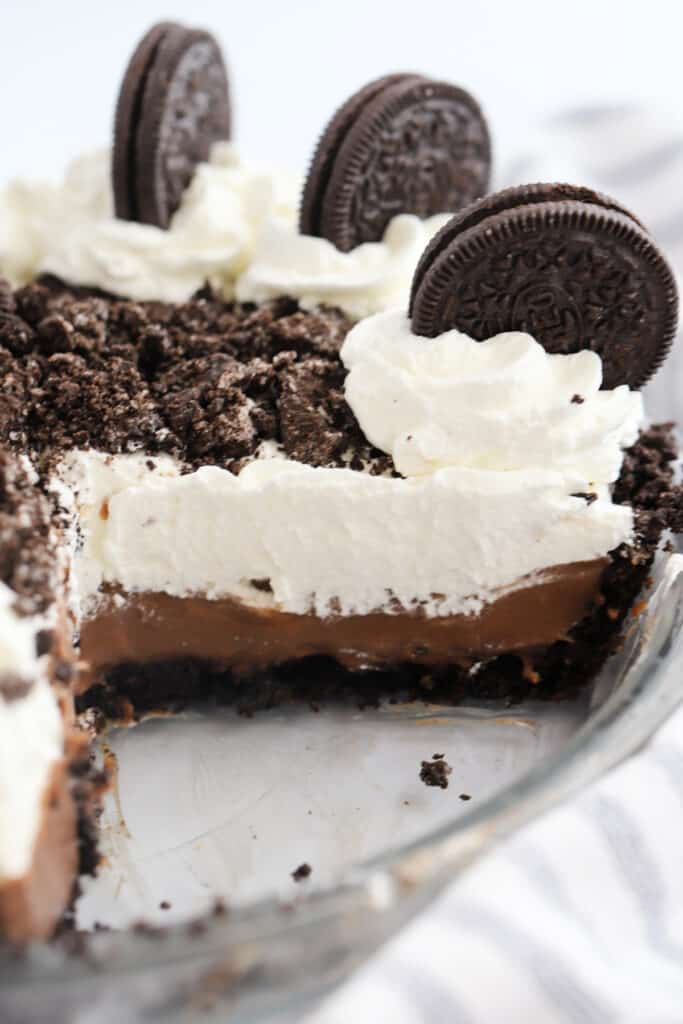 A chocolate cream pie in a pie plate with a slice removed, topped with whipped cream and Oreos.