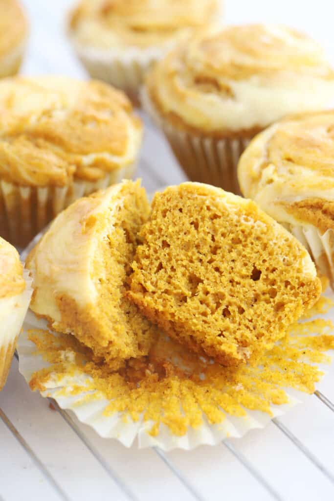 Pumpkin muffins cooling on a wire rack with one opened and cut in half.