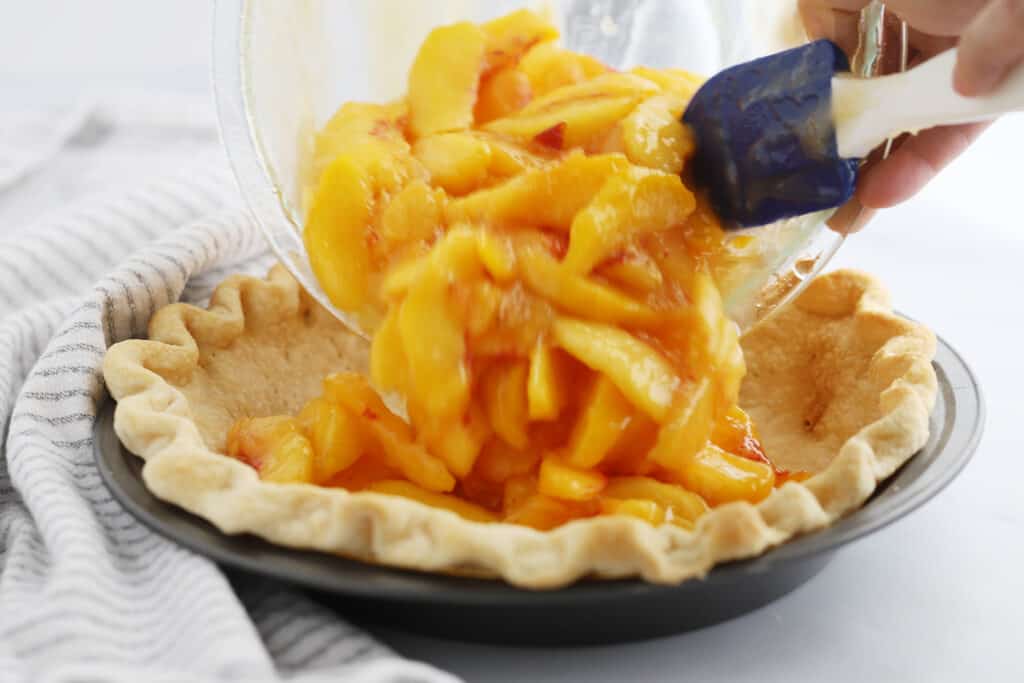 Someone scooping peach filling into a baked pie crust; best peach pie recipe. best peach pie recipe