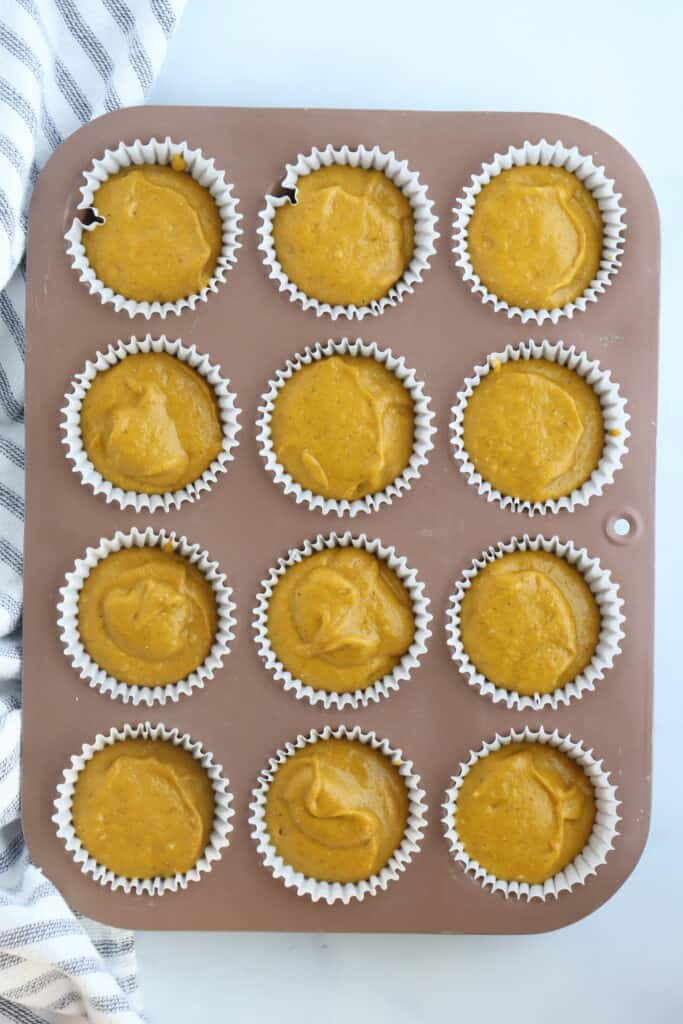 A photo from the top of a muffin pan filled with pumpkin muffin batter. Pumpkin cake mix muffins, pumpkin spice cake mix muffins, pumpkin and cake mix muffins.