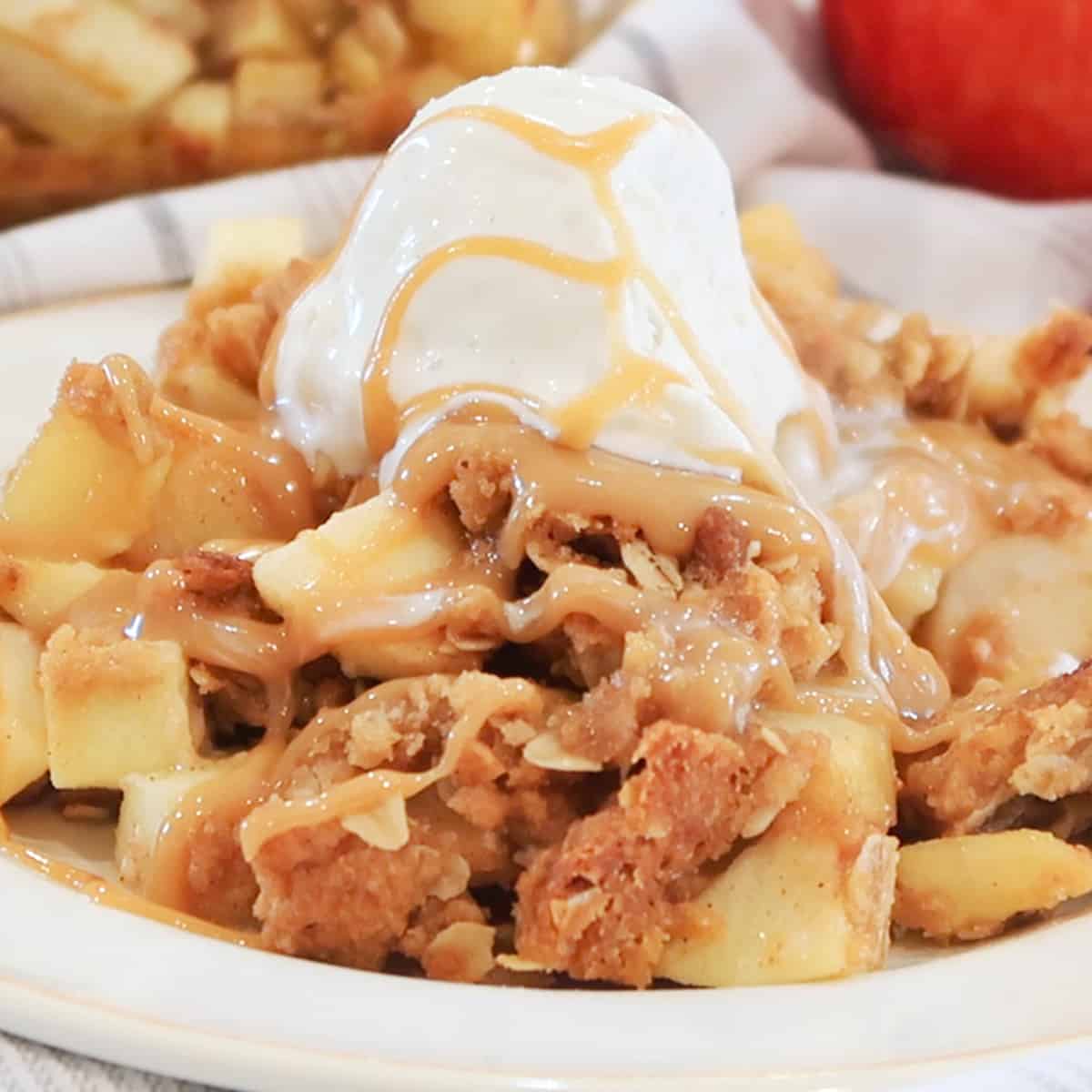 apple crisp recipe, caramel, ice cream and apple crispy on a white plate with apples in the background