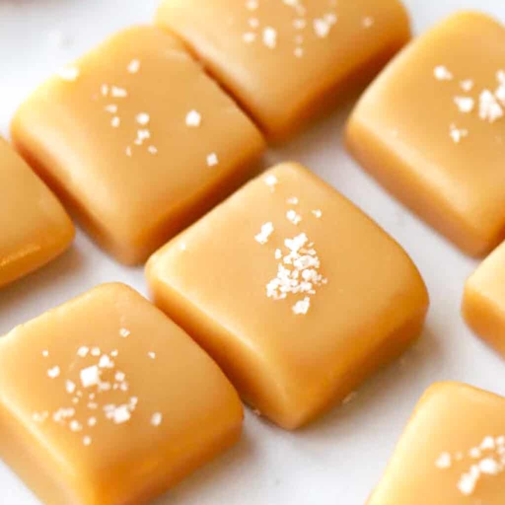 Homemade caramel candies cut into squares and topped with sea salt all lined up on a tray with parchment paper.