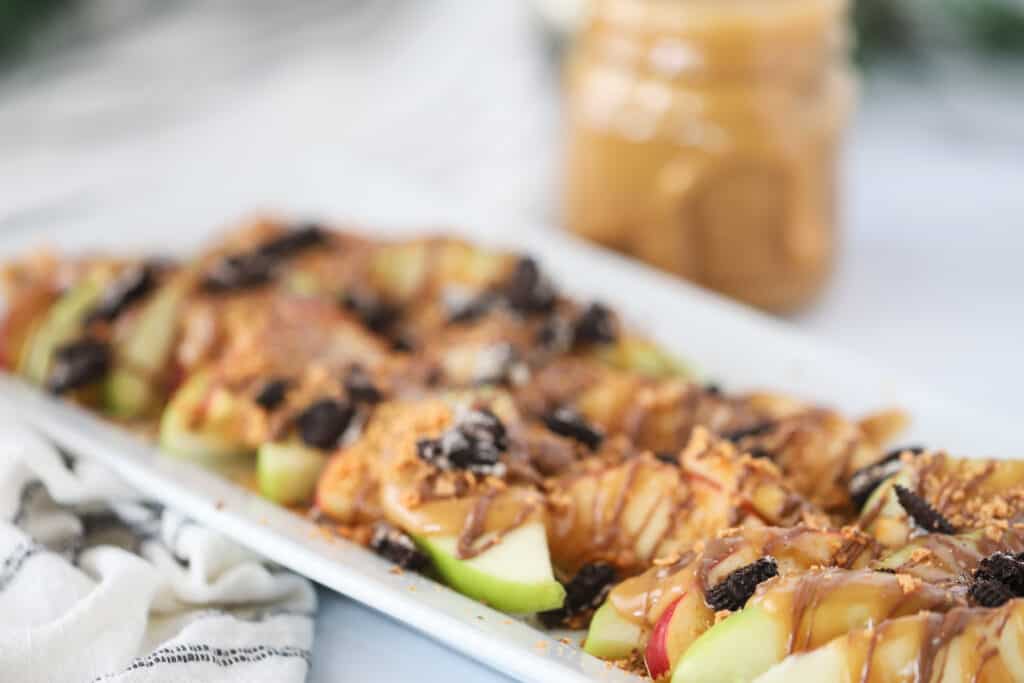 A plate filled with apple nachos, topped with caramel sauce and sweet cookies and candy.