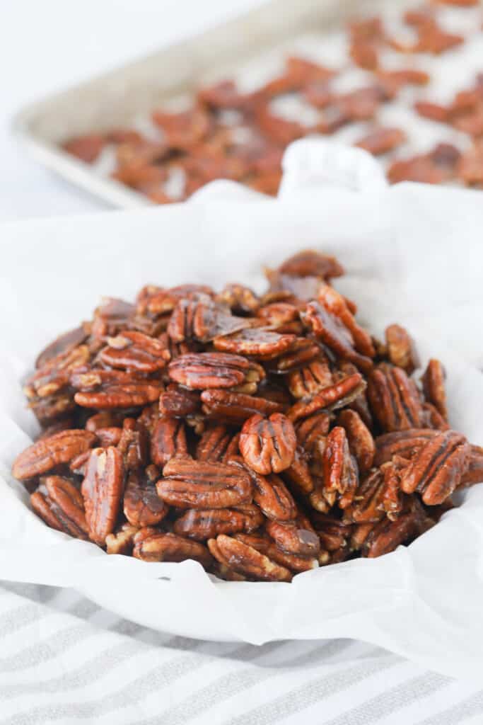A bolw full of candied pecans with a sheet tray full of them behind.