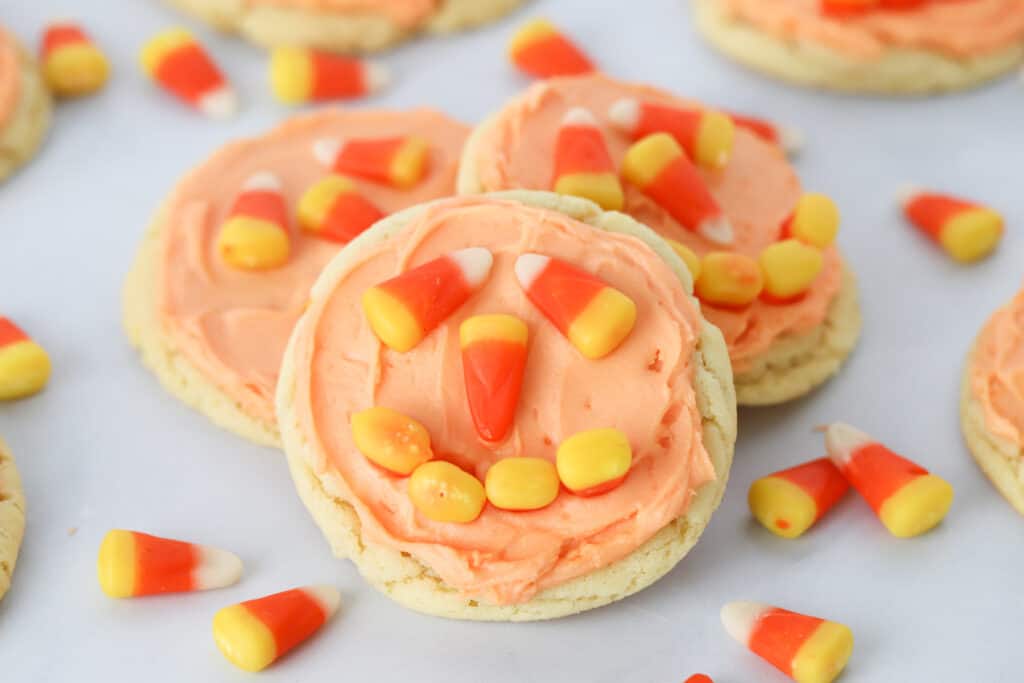 A stack of cookies topped with orange frosting and candy corns to look like jack-o'-lanterns. Jack o lantern cookie recipe.