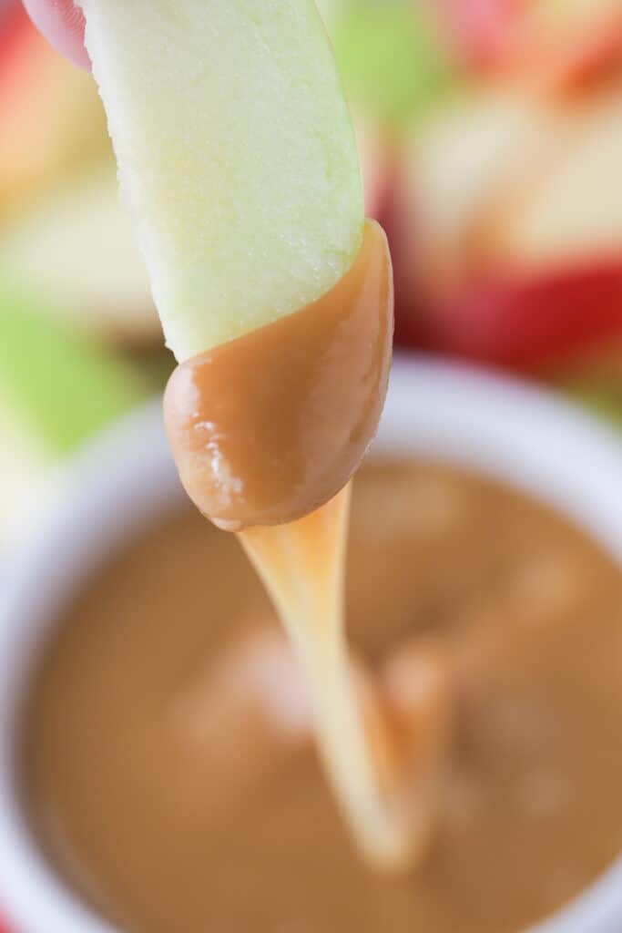 An apple slice with caramel sauce for apples, caramel sauce dripping off of it.