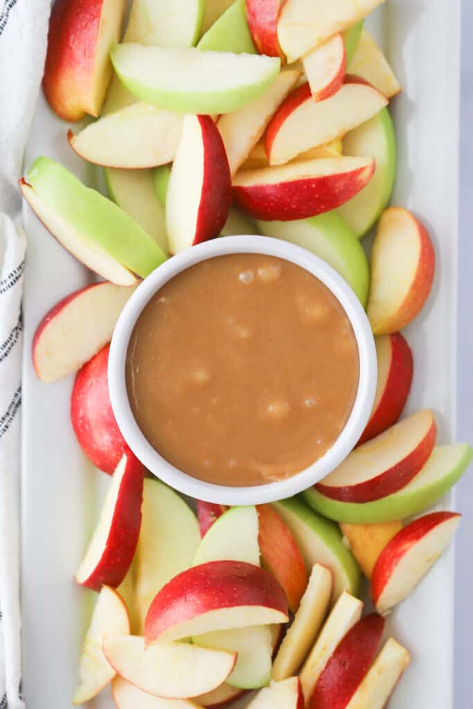 Apple slices arranged on a plate with a bowl of caramel sauce in the center. Caramel apple nachos, easy apple nachos recipe.