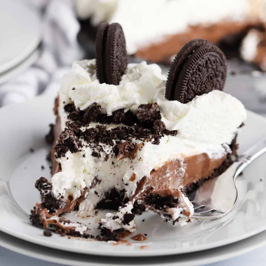 A plate with a slice of chocolate cream pie topped with Oreo cookies and whipped cream.