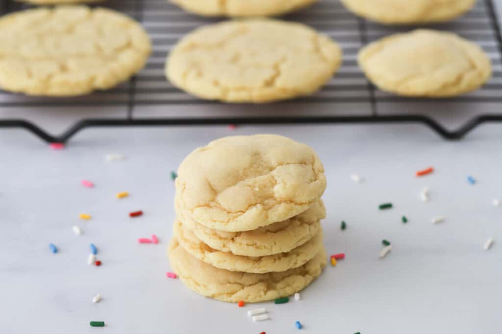 A stack of soft chewy sugar cookies on a table with sprinkles.