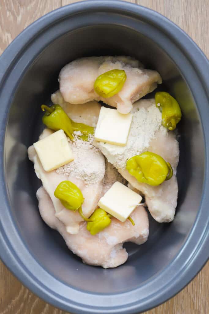 Chicken breasts, pepperoncini, butter and spice mix in the bottom of a crock pot ready to cook. mississipi chicken. Mississippi pot roast chicken. Mississippi crock pot chicken.