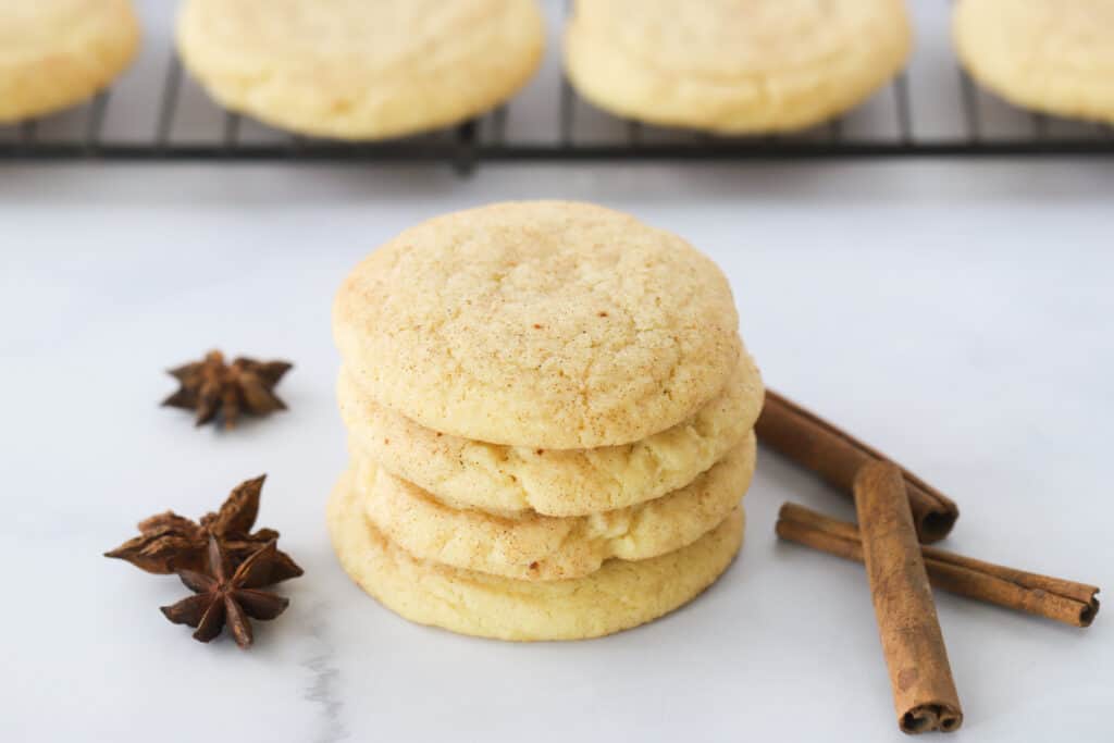A stack of snickerdoodle cookies on a table with cinnamon sticks and star anise.