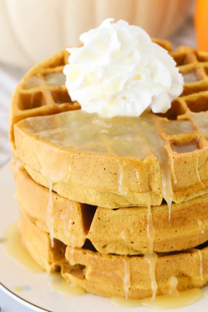 A stack of waffles topped with syrup and whipped cream.