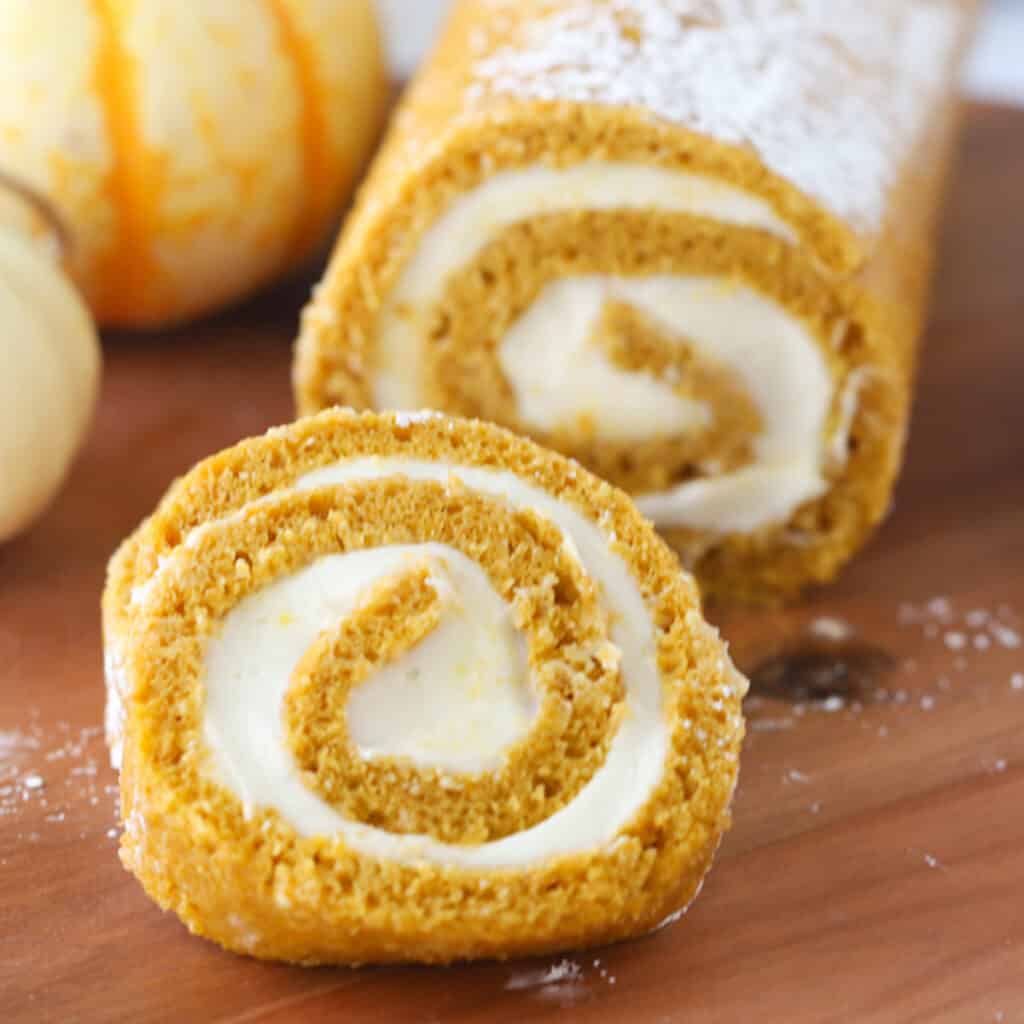 Pumpkin roll with cream cheese frosting on wood cutting board with slices showing.