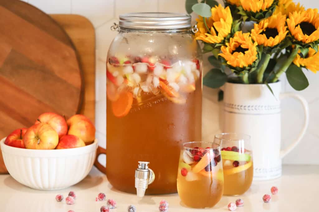 A table with a large pitcher and two individual glasses full of caramel apple punch, next to a bowl of apples. Applepunch. Fall punch recipes.