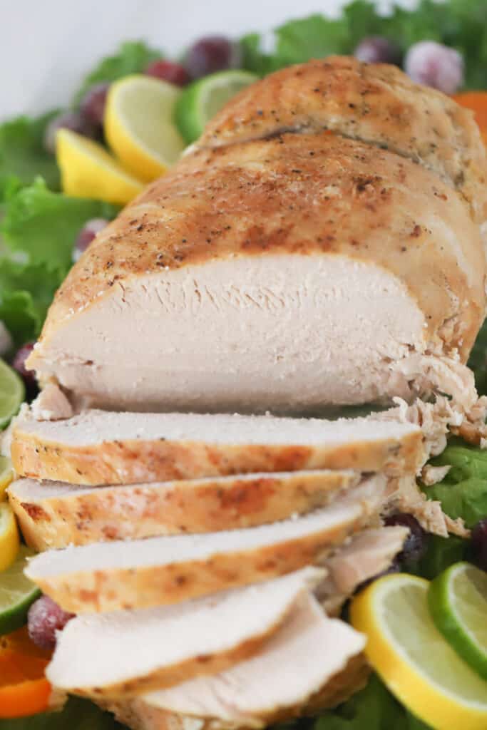 Cooked turkey breast sliced and laying on serving platter with lettuce and other fresh citrus garnish.