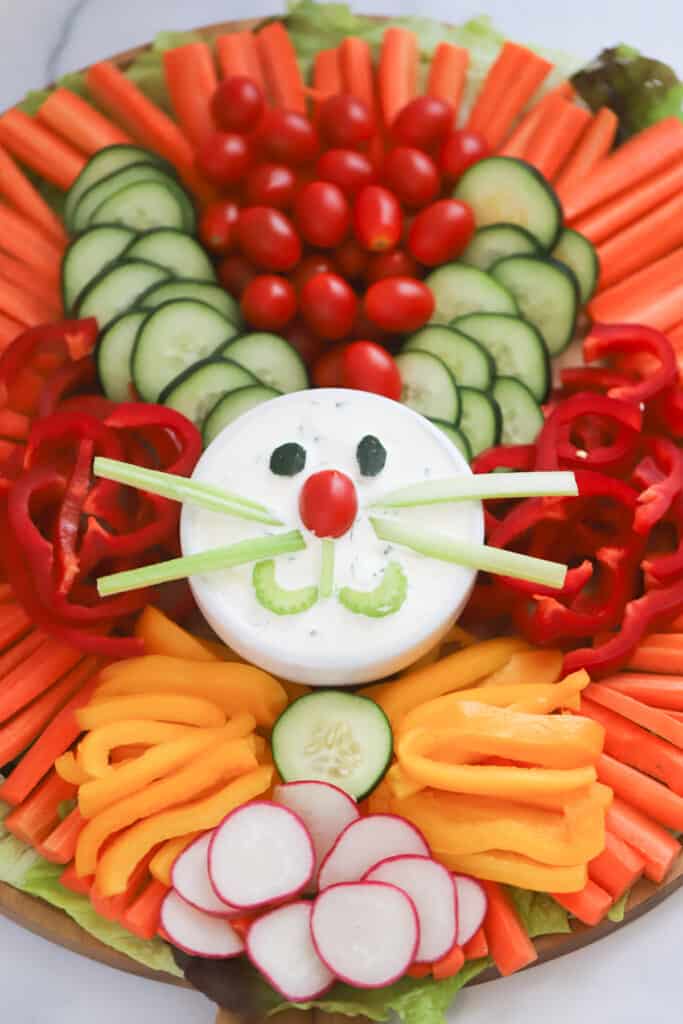 An appetizer tray filled with cut fresh veggies and a container of dip decorated to look like an easter bunny easter veggie tray. rainbow veggie tray, veggie platter ideas. 