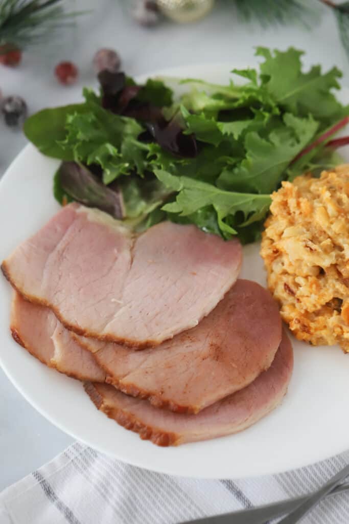 A white dinner plate with servings of spiral sliced ham recipe, salad and mac and cheese.