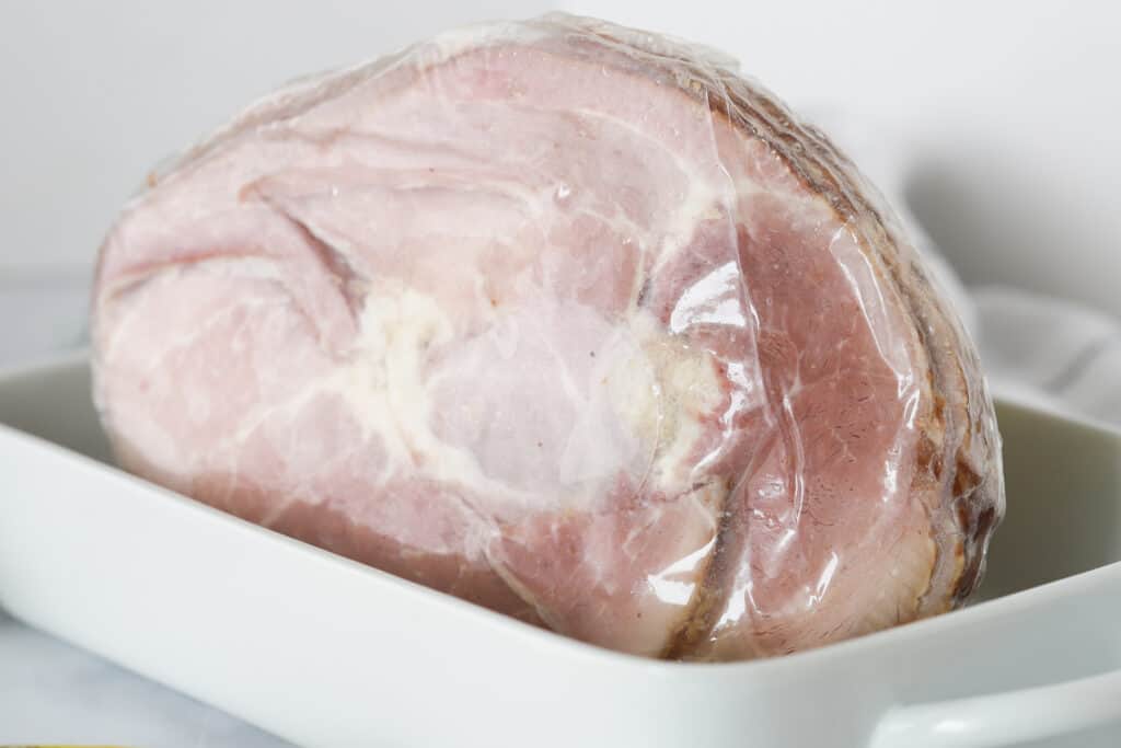 how to cook a spiral ham, a precooked ham still in its packaging inside a baking dish.
