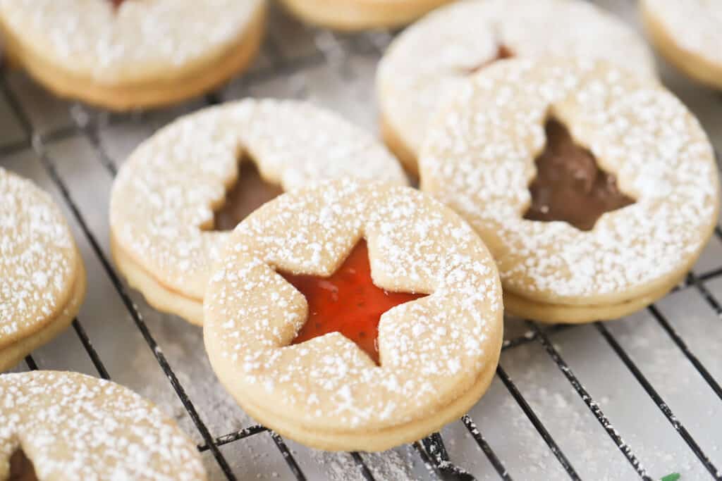 Linzer cookies dusted with powdered sugar resting on a wire rack.