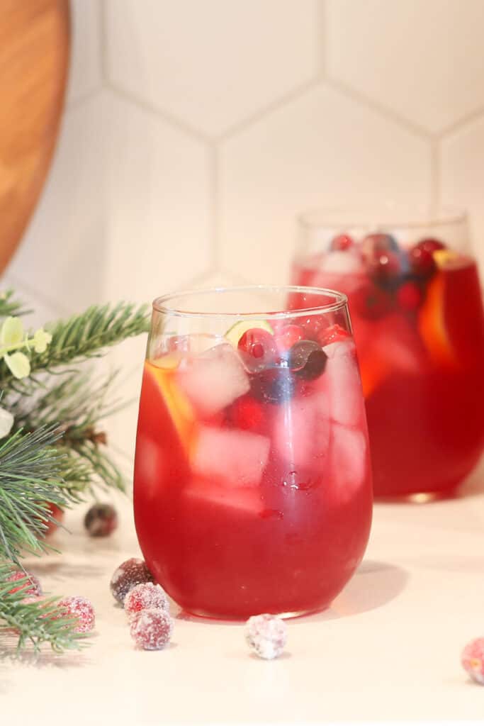 A glass on a table full of red punch garnished with fresh cranberries.