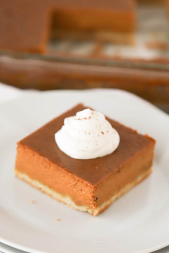 A pumpkin pie square on a white plate topped with whipped cream.