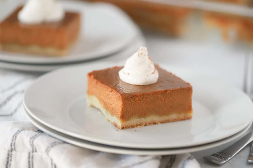 A pumpkin bar on a white plate topped with a dollop of whipped cream.