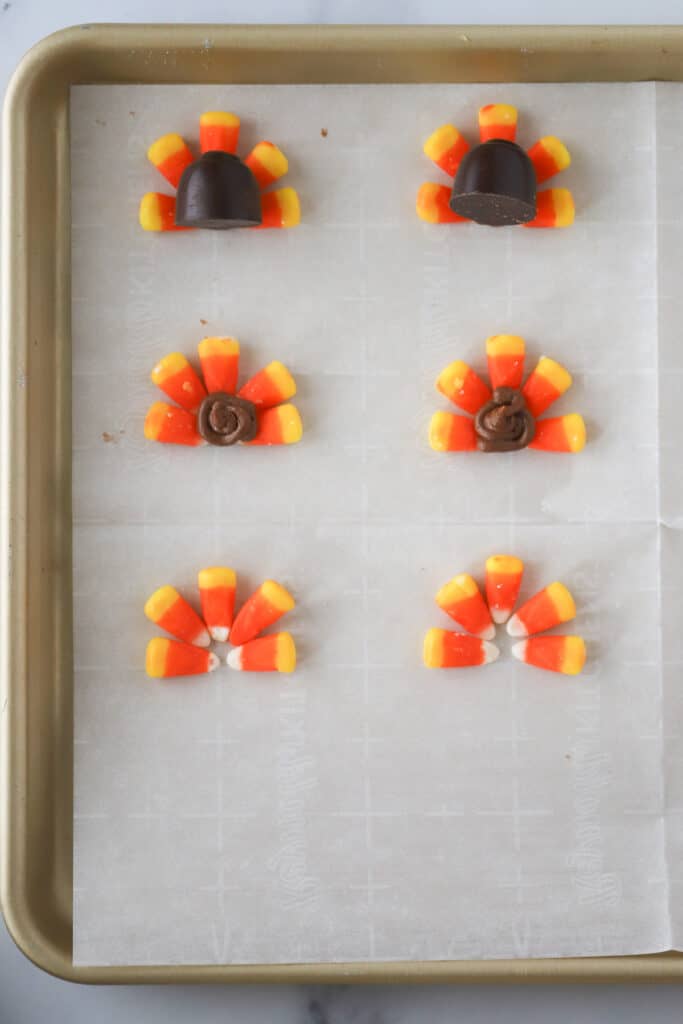 Candy corns arranged on a sheet tray in a fan shape - some with chocolate covered cherries already attached.