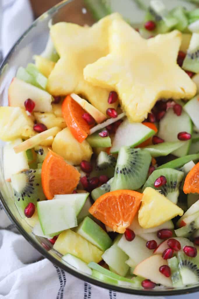 Fruit salad made with kiwi, oranges, pineapples and pomegranate seeds, topped with star-shaped pineapple slices.pomegranate fruit salad. 