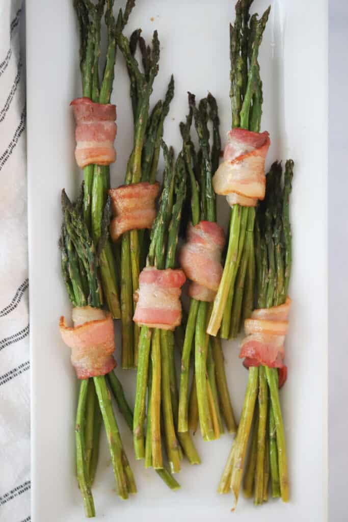 air fryer bacon wrapped asparagus cooked to perfection, on a white serving plate. Unique Brunch ideas