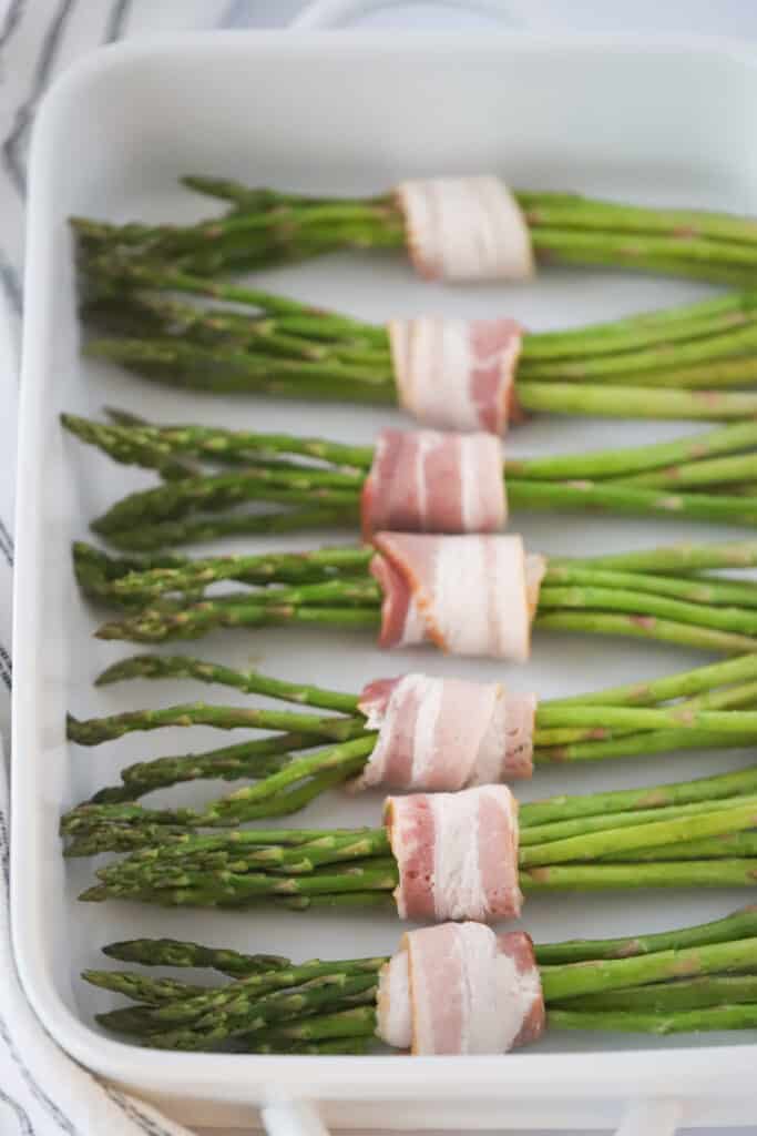 Asparagus bundles wrapped in slices of bacon in a baking dish.