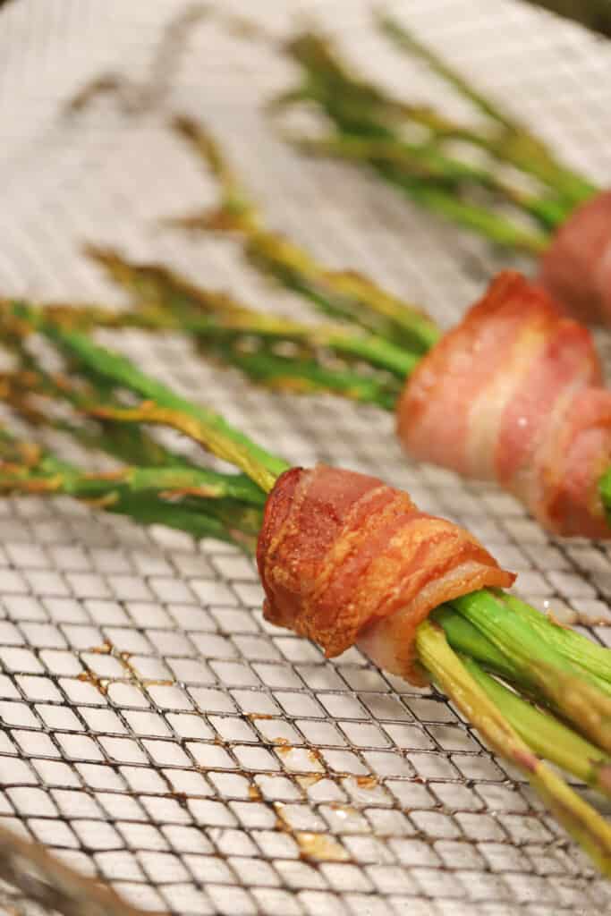 Bundles of asparagus wrapped with crispy bacon on a wire rack.