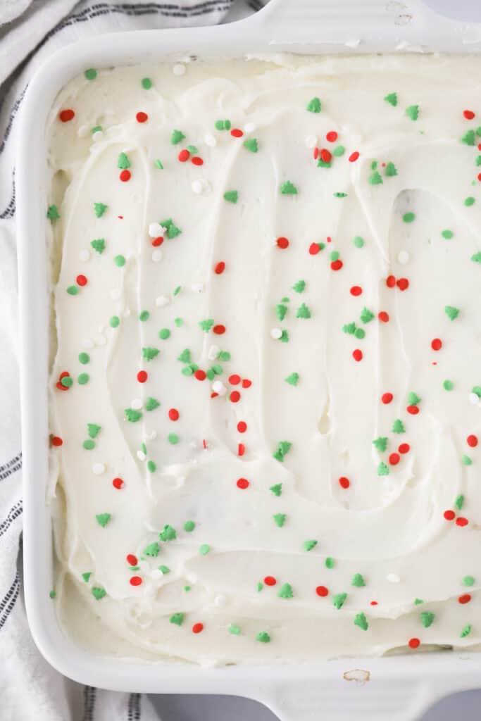 A baking dish with a cake frosted and topped with holiday sprinkles.