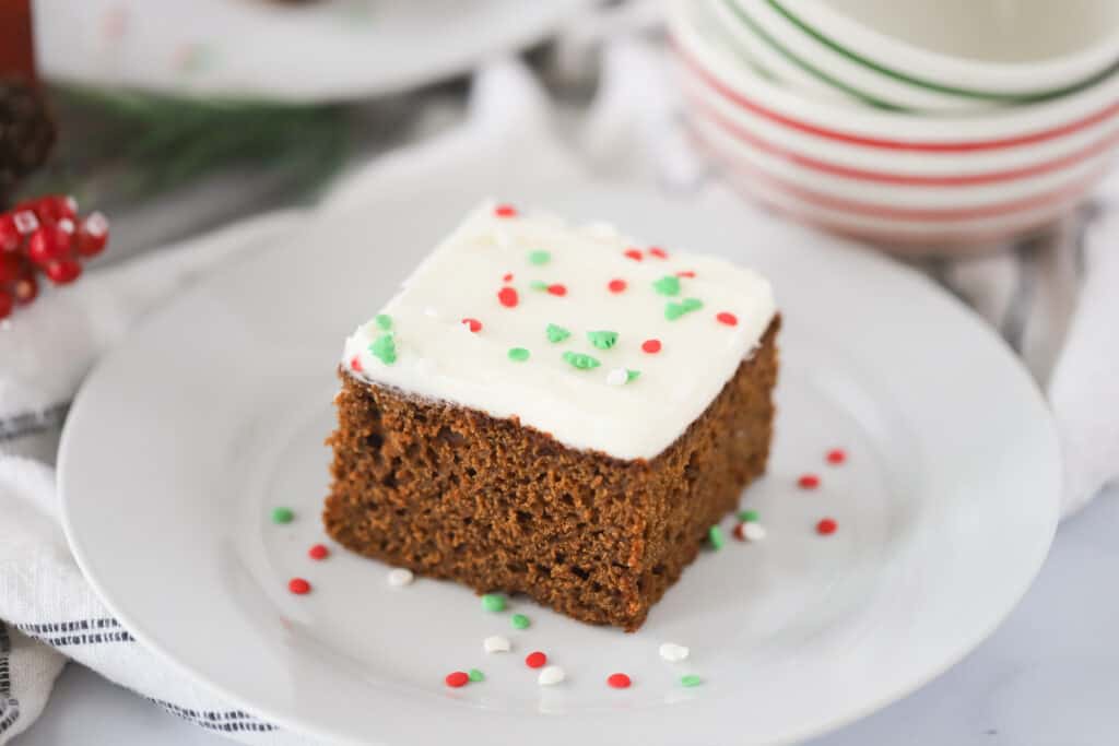 A slice of cake topped with frosting and holiday sprinkles on a white plate.