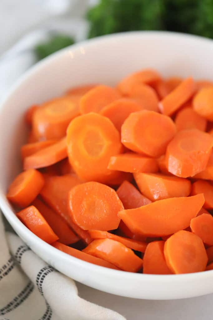 A bowl full of sliced carrots on a table. carrots side dish recipe, brown sugar honey glazed carrots. 