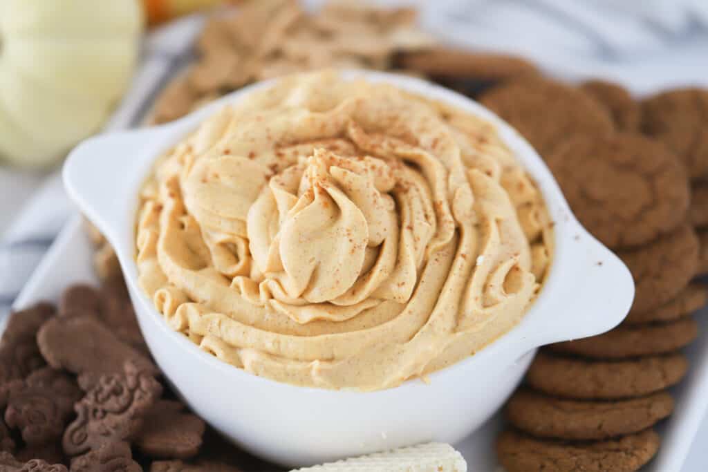 A white bowl filled with whipped dessert dip, on a plate surrounded by cookies.