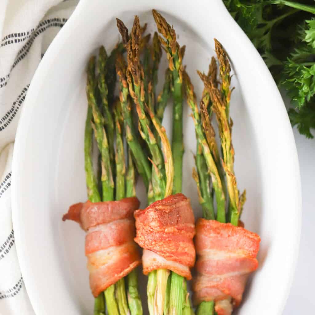 bacon wrapped roasted asparagus bundles on a white serving plate.