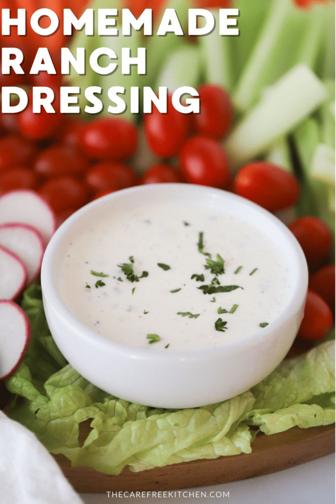 A white ramekin filled with ranch dressing surrounded by fresh raw veggies.