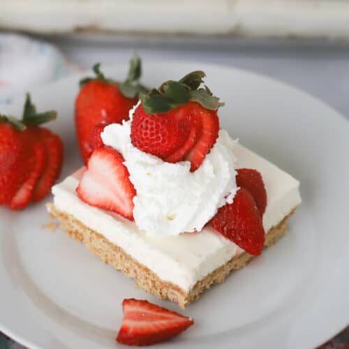no bake cheesecake bars served with strawberries and whipped cream topping
