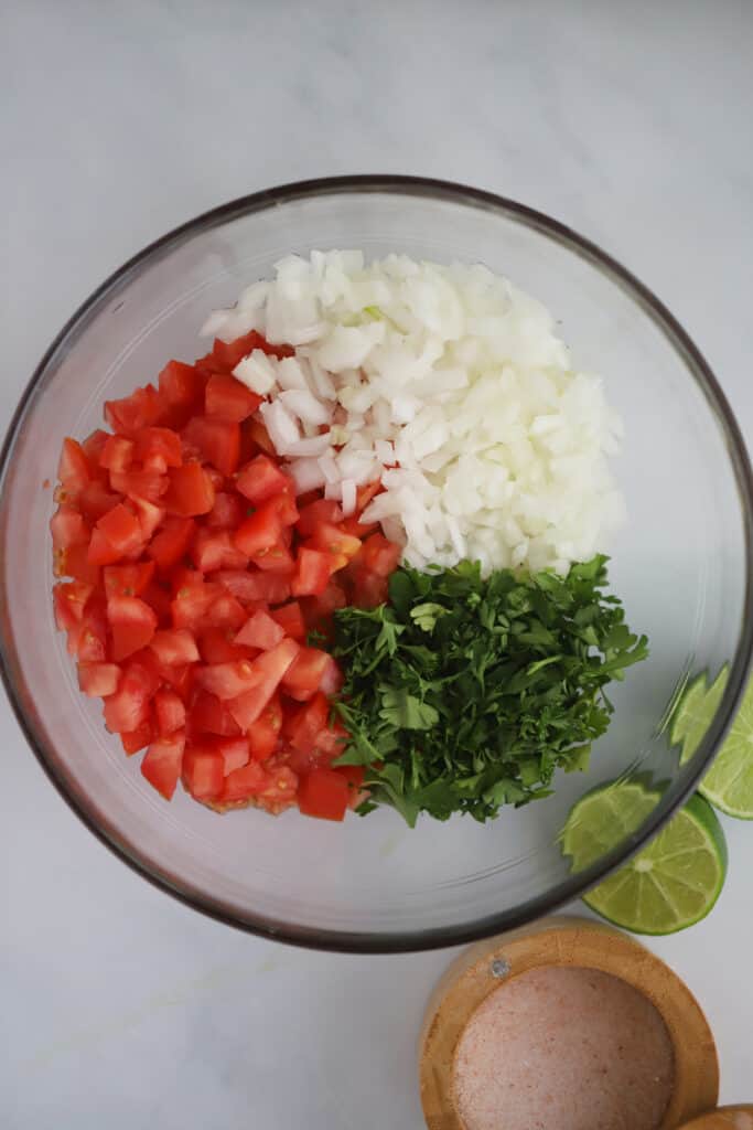A glass bowl with ingredients to make homemade pico de gallo.