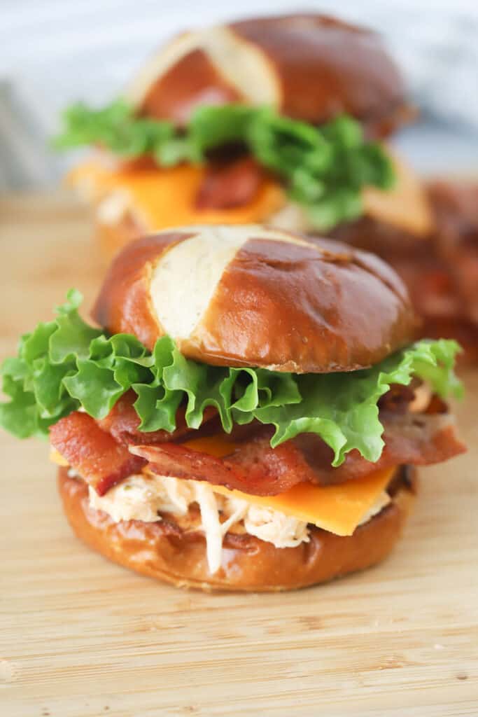 buffalo crockpot chicken sandwich on a table, filled with shredded chicken, cheese, bacon and lettuce. buffalo chicken slow cooker recipe
