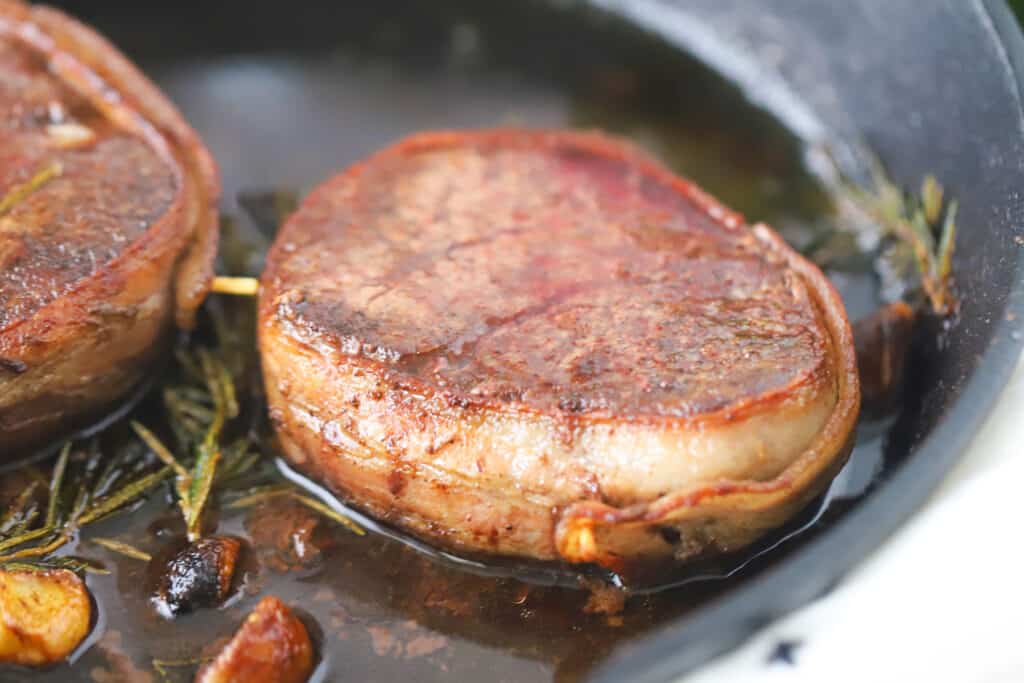 Pan seared filet mignon wrapped with bacon in a cast iron skillet with rosemary and garlic. bacon wrapped filet mignons, filet mignon cut, bacon wrapped steaks, how to cook filet mignon wrapped in bacon