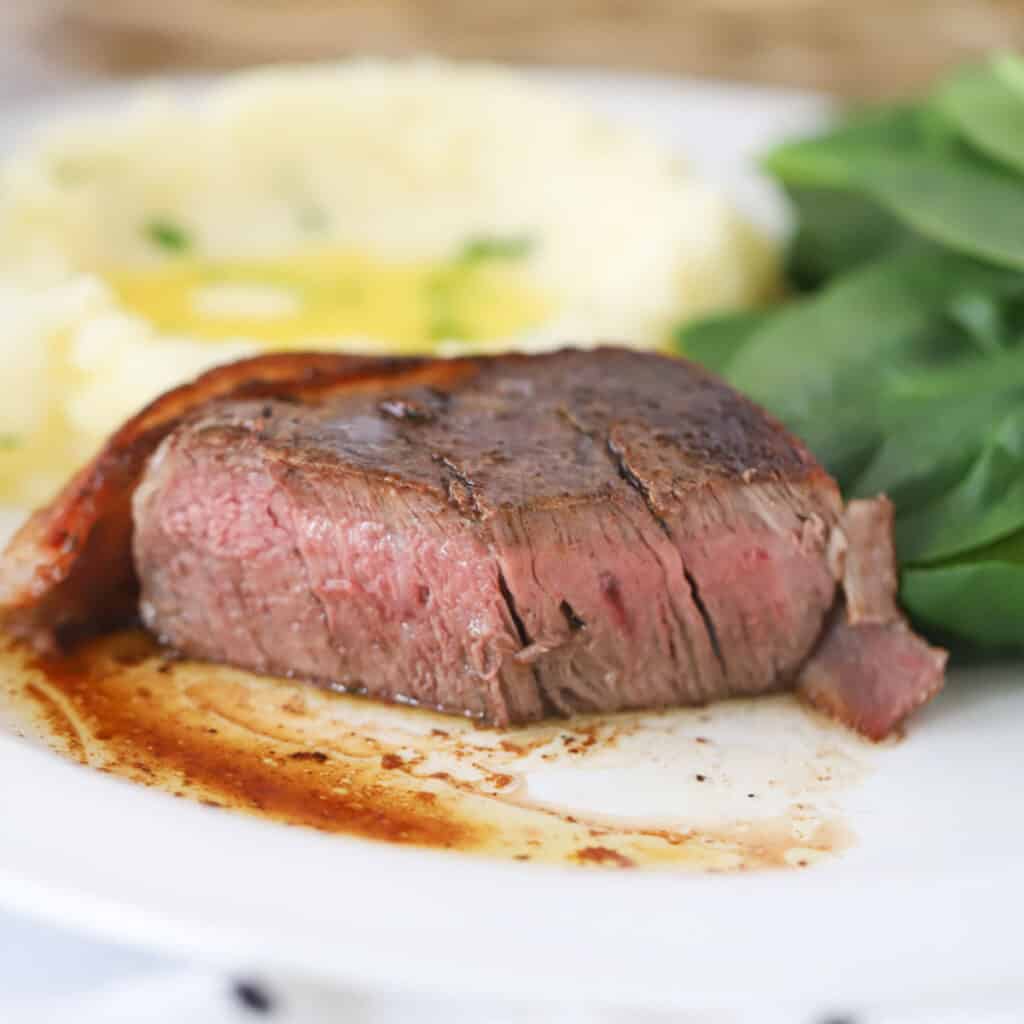 Filet mignon on a white dinner plate with mashed potatoes. Valentine’s day meal ideas. 