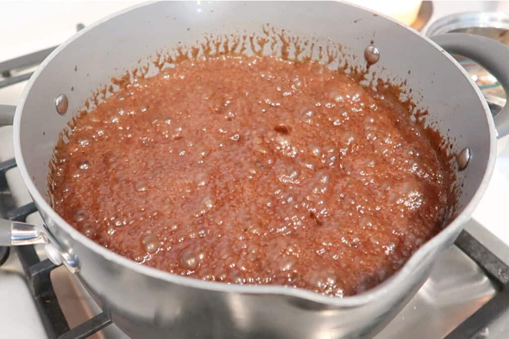 A saucepan with caramel cooking over a stove.