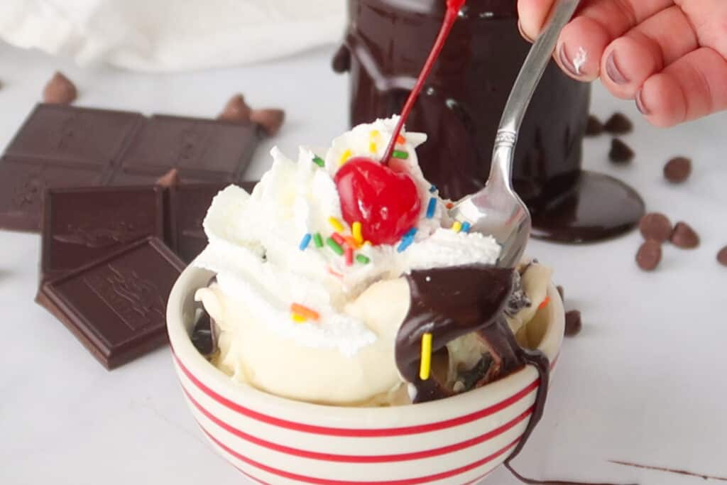A bowl of ice cream topped with whipped cream, a cherry, sprinkles and our Best Hot Fudge Sauce. Hot chocolate fudge.