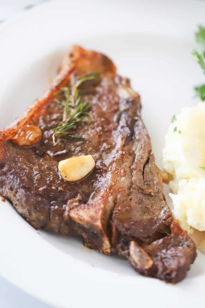 A dinner plate with a Pan Seared Steak topped with rosemary, garlic and a side of mashed potatoes, steak recipes pan.