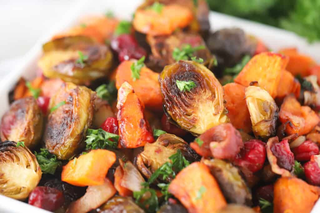 Oven-roasted vegetables in a baking dish including brussels sprouts, sweet potatoes and onions.
