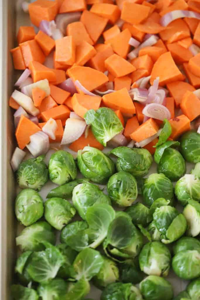A sheet tray with halved brussels sprouts and diced onions and sweet potatoes. roasted sweet potatoes and Brussels sprouts.