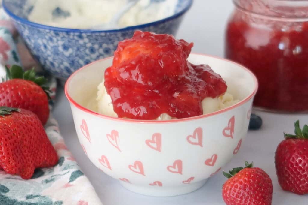 A bowl full of vanilla ice cream topped with homemade Strawberry Sauce, strawberry sauce  with frozen strawberries.