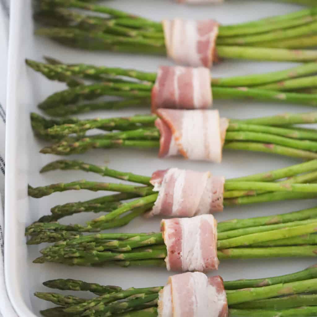 air fryer bacon wrapped asparagus on a white serving plate.