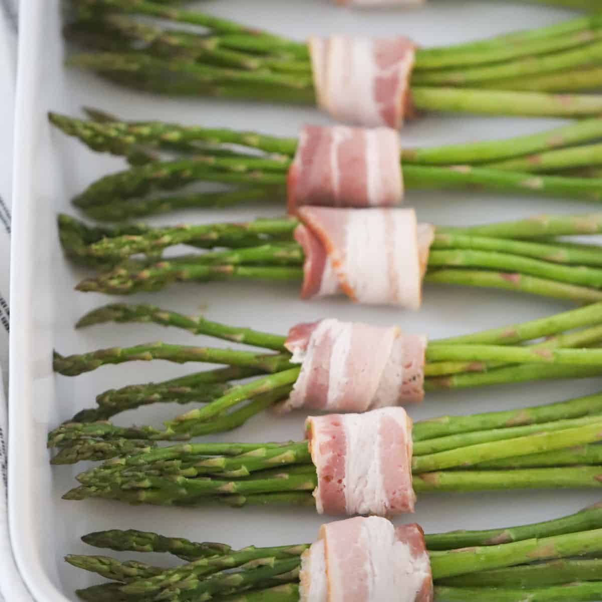 air fryer bacon wrapped asparagus cooked to perfection, on a white serving plate.